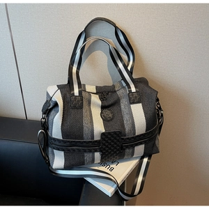Detail view of large striped travel bag with black leather trim and woven shoulder strap
