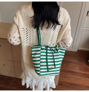 Detail of green and white striped canvas tote bag with silk ribbon bow and metal nameplate