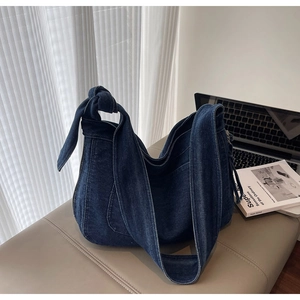 Detailed view of dark blue denim tote bag with stylish knot strap on a beige stool