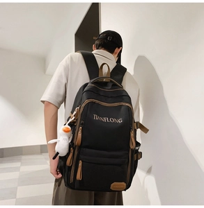 Detail of black backpack with brown trim, side buckle and cute duck plush charm accessory