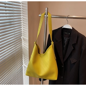 Close-up of a yellow lychee pattern leather tote bag hanging on a metal hanger with shadow