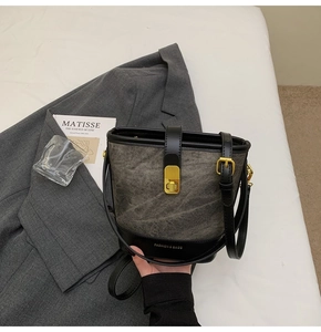 Détail du sac seau vintage gris avec garniture en cuir noir et boucle dorée sur le lit