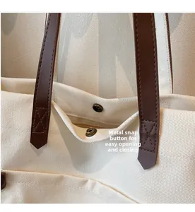 Detail of canvas tote bag featuring brown leather strap with X-stitch and metal snap closure
