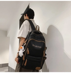 Detail view of black high-capacity backpack with brown leather accents and plush charm