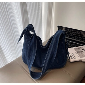 Detail of a deep blue denim tote bag featuring a unique knotted strap and sleek metal zipper