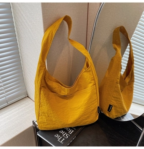Detail of yellow nylon tote bag with pleated texture and wide shoulder strap shown in a mirror