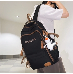Close-up of black canvas backpack with brown leather trim and white duck plush keychain