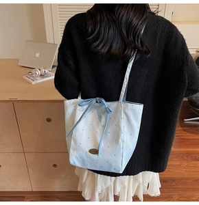 Detail of light blue polka dot fabric tote bag with a handmade metal plate and bow