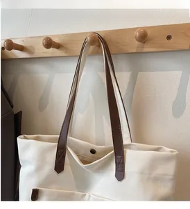 Close-up of cream canvas tote bag with brown leather handles and metal snap button detail