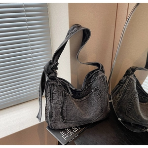 Detail of dark grey washed denim hobo bag with stylish knotted shoulder strap and front pocket