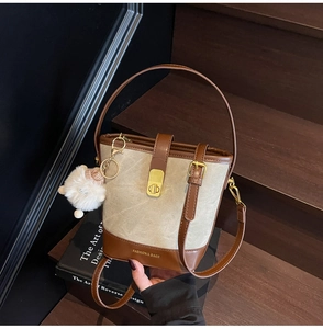 Détail du sac seau bicolore en toile beige avec base en cuir marron et fermoir rotatif doré