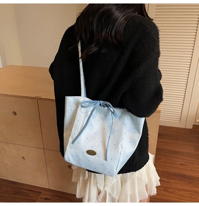 Detail showing light blue polka dot tote bag texture and navy bow on a model's shoulder
