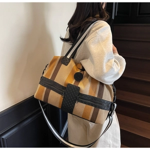 Detail of striped canvas travel bag showing front zipper pockets and leather logo patch
