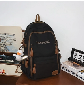 Detail of black nylon backpack with brown leather trim and cute plush duck accessory