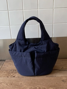 Navy blue nylon bucket tote bag with dual front pockets on a rustic wooden tabletop
