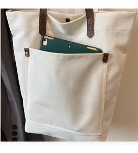 Detail of canvas tote bag front pocket showing storage capacity for a green tablet