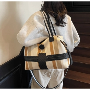 Rear view of model carrying a striped canvas travel bag with leather trim and shoulder strap