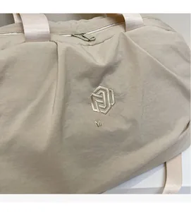 Detail showing the cream nylon fabric texture and embroidered logo on the travel bag