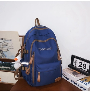 Navy nylon backpack with brown trim and side duck plushie charm on a wood table