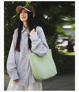 Close-up of light green canvas tote bag with front pocket in natural outdoor setting