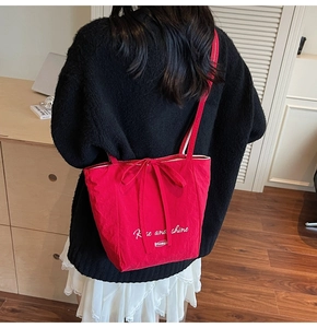 Detail of red canvas tote bag featuring white Rise and shine text and bow ribbon closure