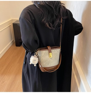 Détail du sac seau gris avec base en cuir marron et breloque pompon en peluche