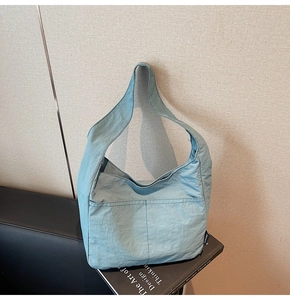 Close-up of minimalist teal nylon tote bag with functional front pockets on a book