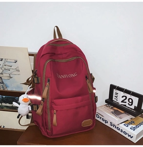 Detail of burgundy backpack showing polished hardware, brand logo, and a plush duck charm