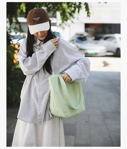 Close-up of light green canvas tote bag with front pocket shown in an outdoor setting
