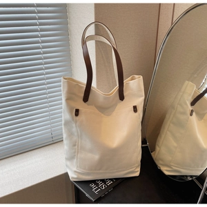 Detail view of canvas tote bag with brown leather handles and rivets in soft natural light