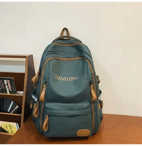 Detail of green nylon backpack featuring brown leather accents and multi-zippered pockets