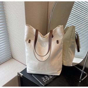 Detail of canvas tote bag showing cream fabric texture, brown leather handle, and rivet