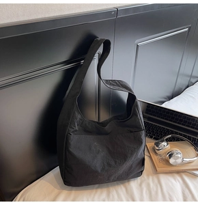 Detail of black nylon tote bag with wide strap and front pocket in a lifestyle setting