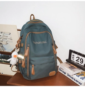Detail of dark green backpack with brown zipper accents and white plush duck pendant