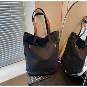 Detail of a black canvas tote with brown leather handles and vintage metal rivets