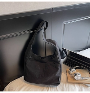 Detail of a large black tote bag with wide shoulder strap on white bedding scene