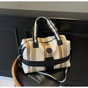 Detail of striped travel tote bag with multi-zipper pockets and woven handles on a chair