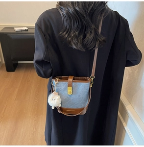 Détail du sac seau en denim bleu avec garniture en cuir brun et breloque mouton
