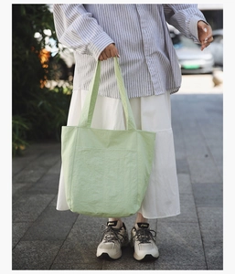Pale mint green nylon tote bag with front pocket shown in a lifestyle outdoor setting
