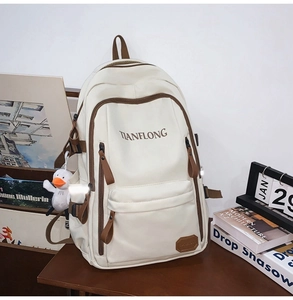Detail of cream white backpack featuring multi-layer storage and a cute duck pendant