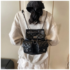 Rear view of a black quilted leather backpack with silver chains on a female model