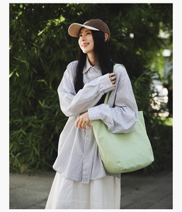 Close-up of a light green canvas tote bag carried by a model in a natural bamboo setting