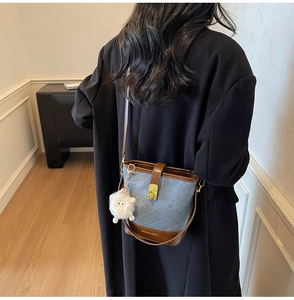Détail du sac seau en denim bleu avec garniture en cuir marron et charmant agneau en peluche