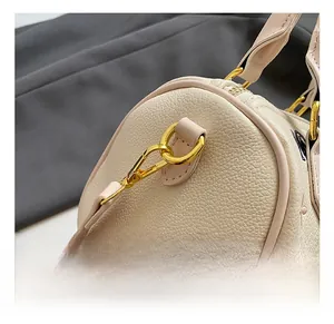 Detail showing the golden metal hook and litchi grain leather of the beige bucket bag