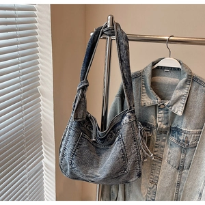 Detail of acid wash denim tote bag showing adjustable knot strap and large front pocket
