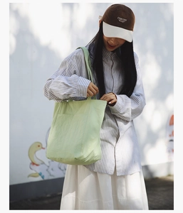 Outdoor view of a minimalist large green canvas tote bag styled with a casual summer outfit