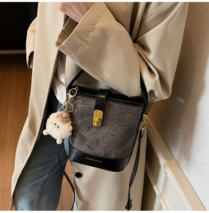 Vue détaillée du sac seau bicolore avec fermoir doré et breloque mouton sur trench beige