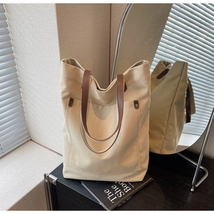 Close-up of beige canvas tote with brown leather straps and front pocket detail