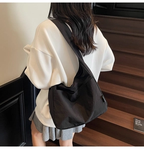 Detailed view of a large black canvas hobo bag with a wide shoulder strap on a model