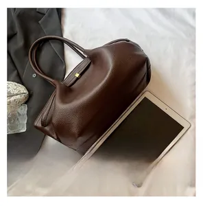 Detail of dark brown leather tote bag with cylindrical handles and metal buckle closure